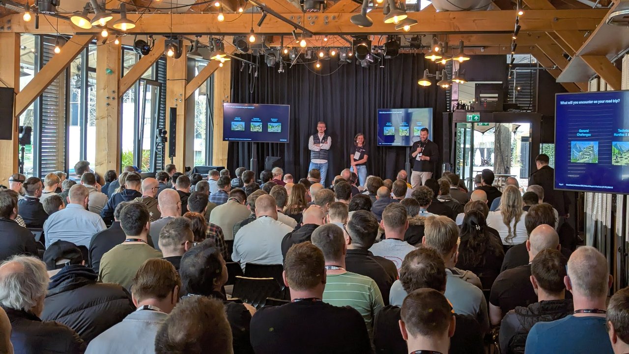 Three speakers on stage at OpenShift Commons Gathering Amsterdam 2026 with the Siemens slide What will you encounter on your road trip on the screens