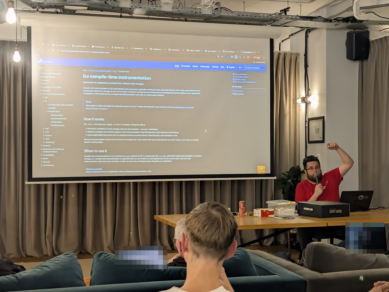 The opentelemetry.io Go compile-time instrumentation page on screen, explaining how the otelc tool hooks into the Go build, with the speaker gesturing at the desk