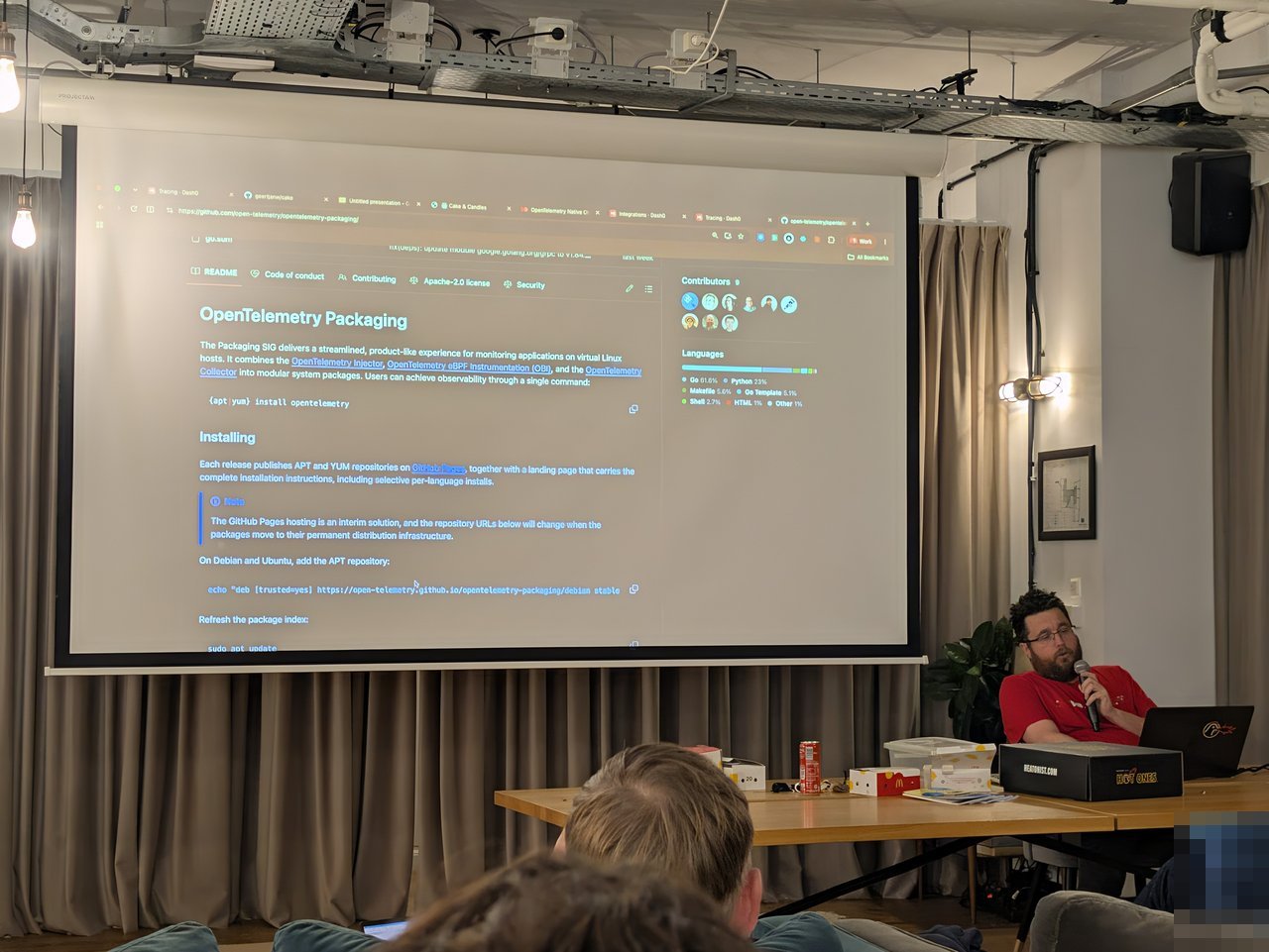 The OpenTelemetry Packaging README on the big screen, describing the Packaging SIG combining the OpenTelemetry Injector, OBI and the Collector into system packages