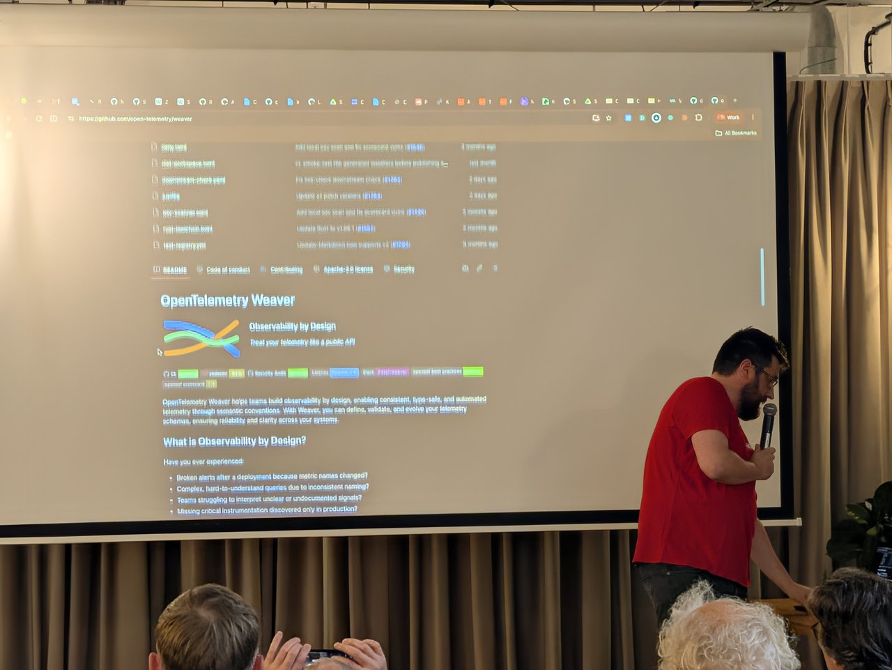 The OpenTelemetry Weaver GitHub README on the big screen, showing Observability by Design and the list of problems it solves, with the speaker beside the screen