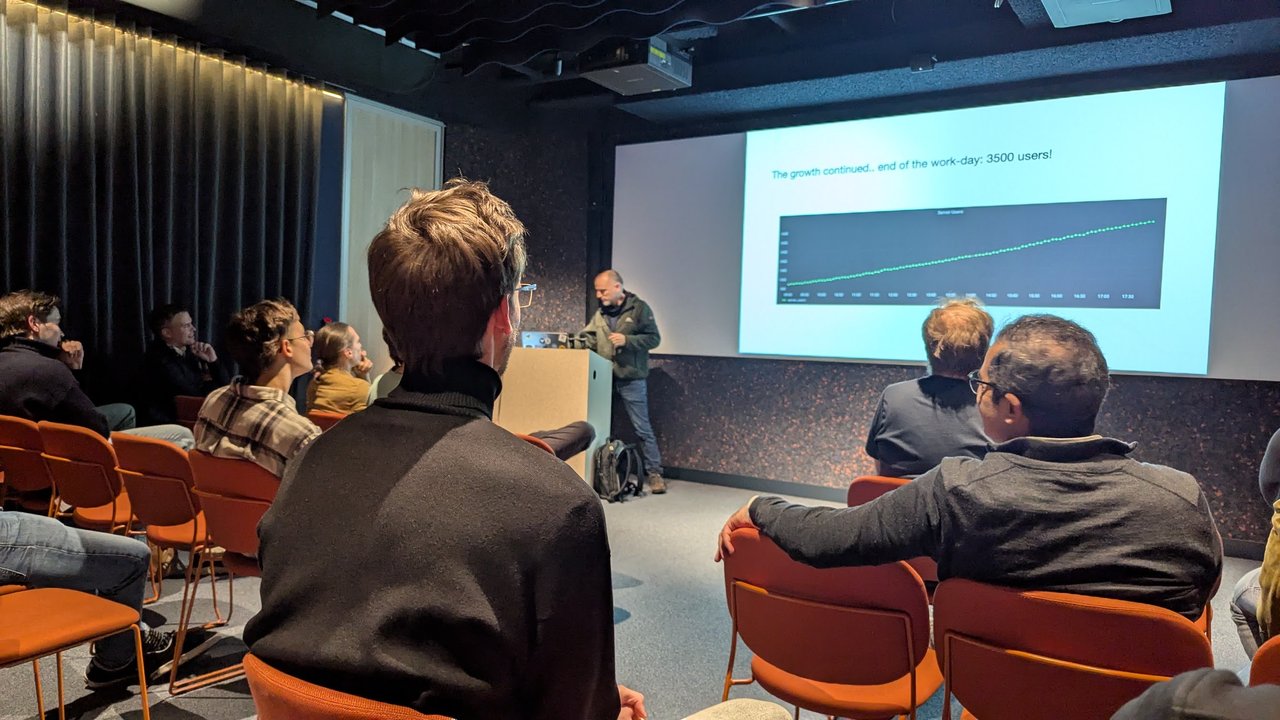 Speaker at the lectern next to a slide reading The growth continued, end of the work-day: 3500 users, above a steadily rising server users graph
