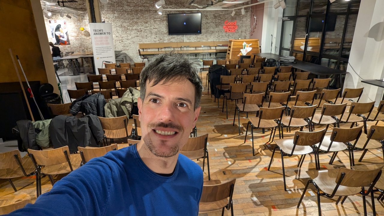 Luca Berton in the empty Picnic canteen in Amsterdam before the developer experience meetup, with rows of chairs and the Good morning Picnic neon sign