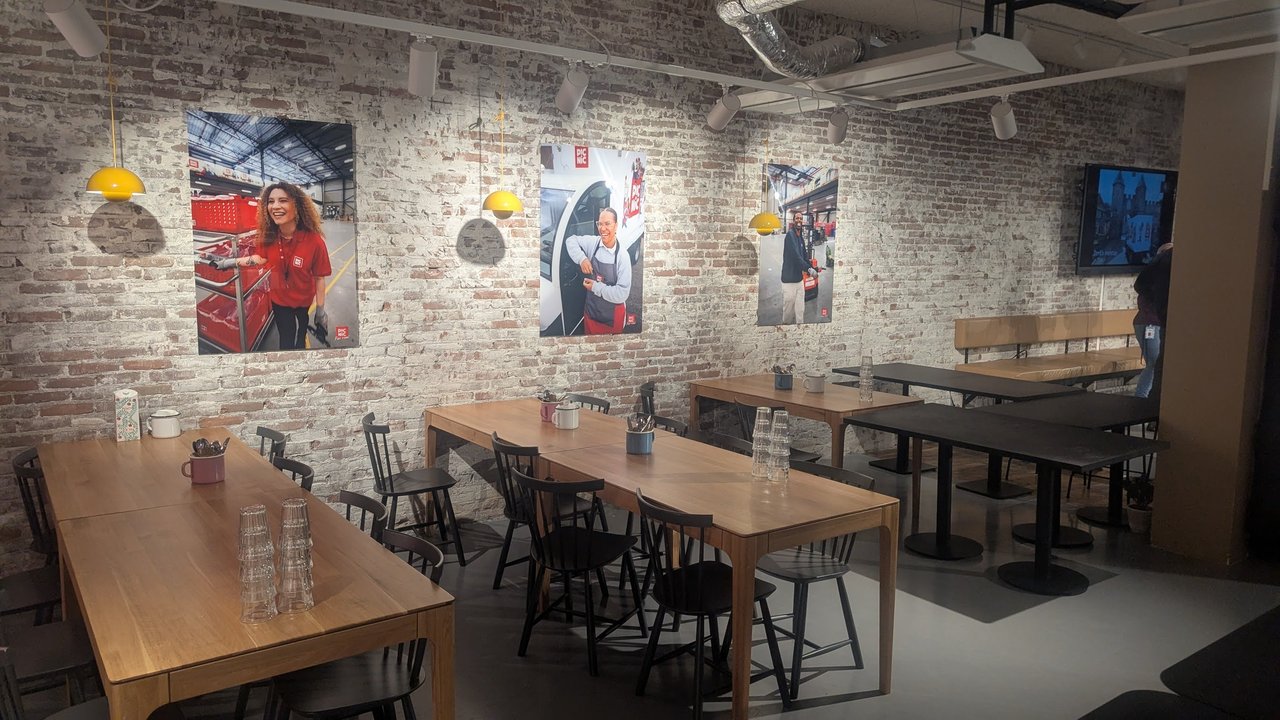 Dining area at Picnic in Amsterdam with long wooden tables, stacked glasses and posters of Picnic delivery staff on a brick wall