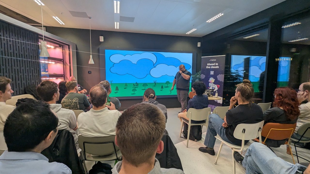 A speaker presents in front of a cartoon slide of clouds over a green landscape with trees, next to the tarmac Ahead in the clouds roll-up