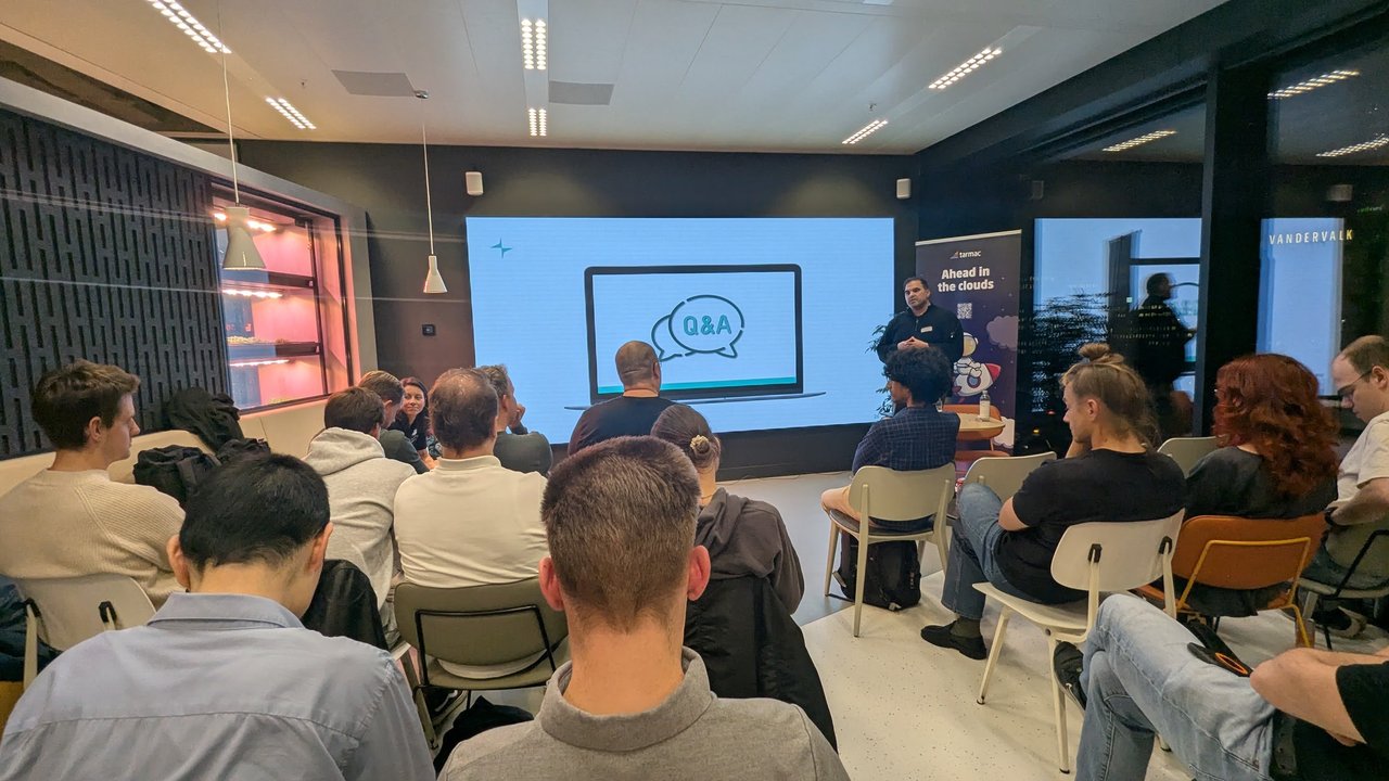 Q&A slide on the screen at Platform Engineering Amsterdam in November 2025, with the speaker standing next to the tarmac Ahead in the clouds roll-up and the audience seated
