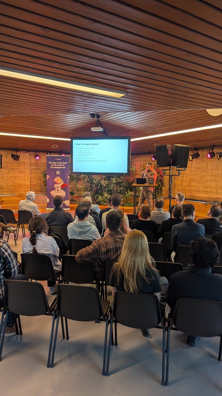 The audience at Tolhuistuin facing the What Is an Agent Harness? slide, with the speaker at the lectern and a tarmac roll-up banner on the left