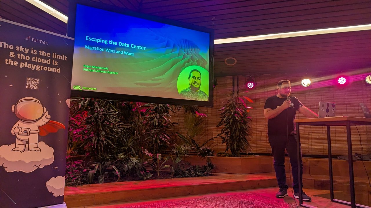 Dejan Mladenovski at the lectern beside his title slide, Escaping the Data Center: Migration Wins and Woes, Principal Software Engineer, Netcetera
