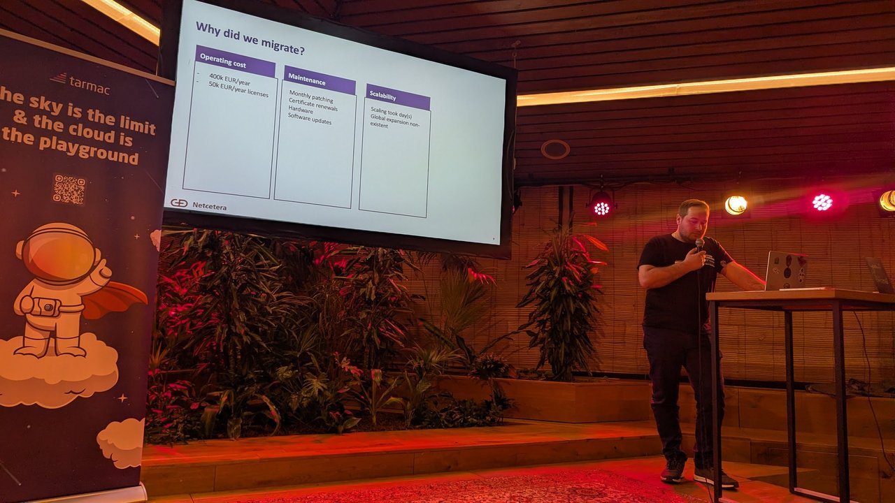 Dejan Mladenovski at the lectern beside the Why did we migrate? slide listing operating cost, maintenance and scalability reasons, Netcetera logo bottom left