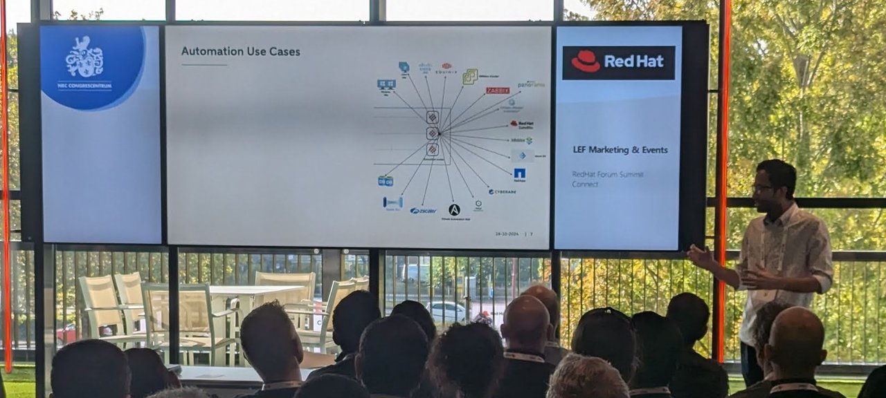 A speaker in front of an Automation Use Cases slide showing a hub-and-spoke diagram of integrations, in a breakout room with windows onto trees