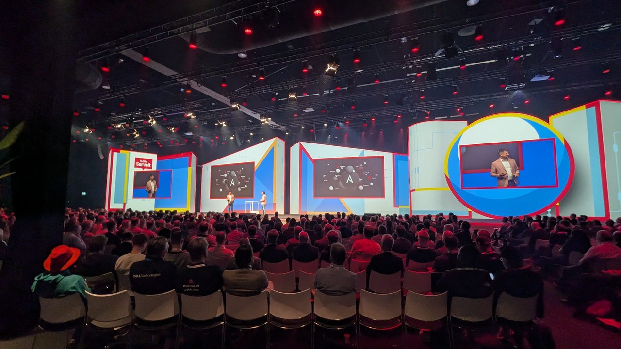 The main theatre at Red Hat Summit Connect Utrecht 2024 seen from the back, with a full audience and the Ansible logo on the stage screens
