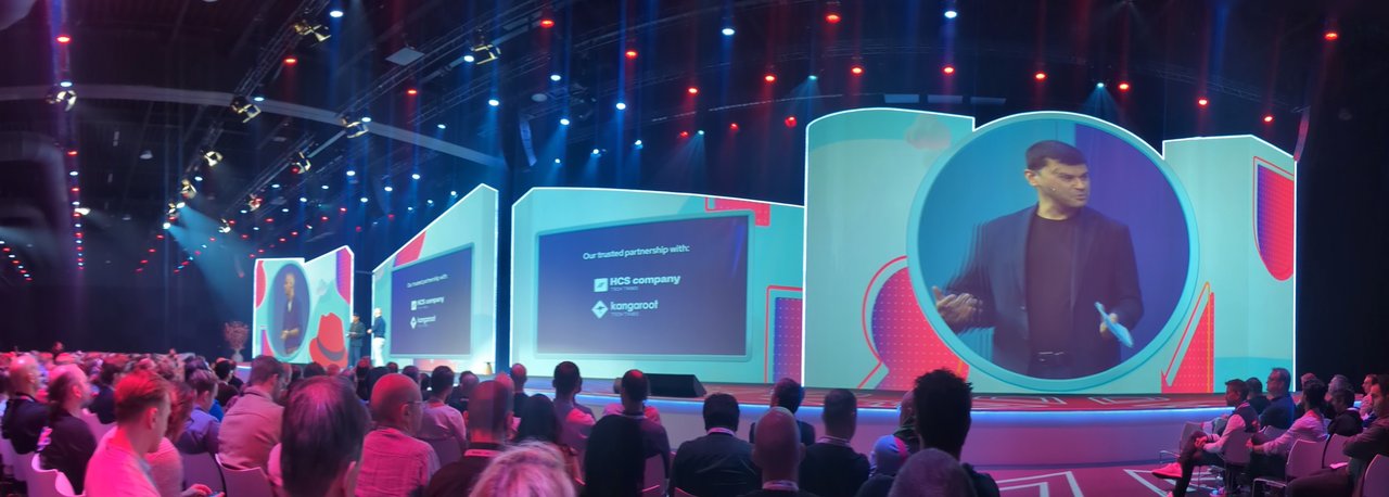 The main stage at Red Hat Summit Connect Utrecht 2025, with a full audience, a speaker on the video wall and a slide listing HCS company and Kangaroot as trusted partners