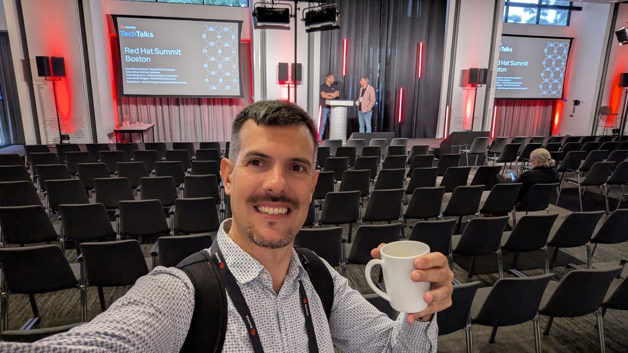 Selfie in the empty main hall at Red Hat Tech Day, with two speakers and a Red Hat Summit Boston slide on the stage behind