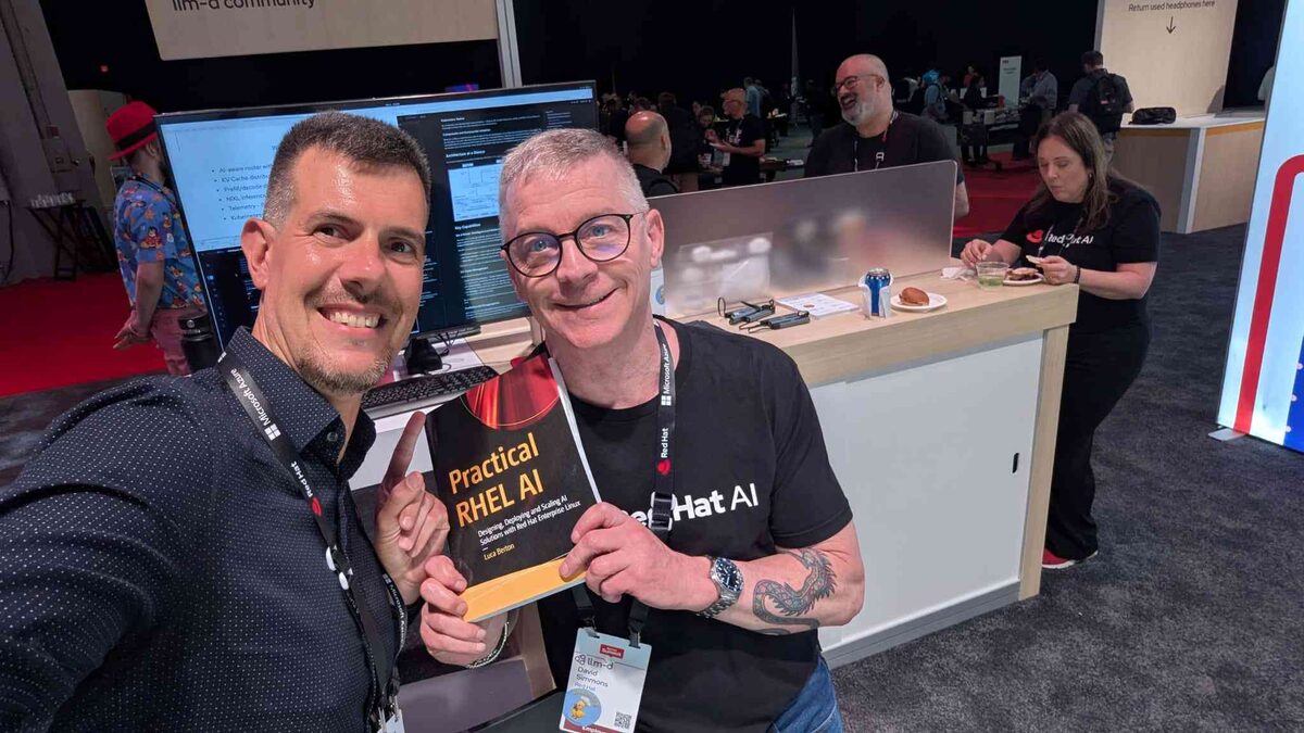 Luca with David Simmons at the llm-d community booth holding Practical RHEL AI
