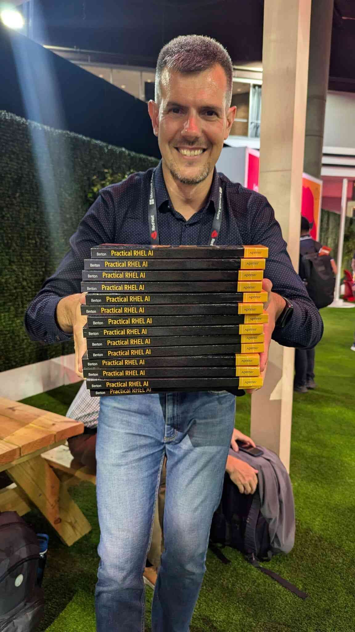 Luca Berton holding a stack of 14 Practical RHEL AI books at Red Hat Summit 2026