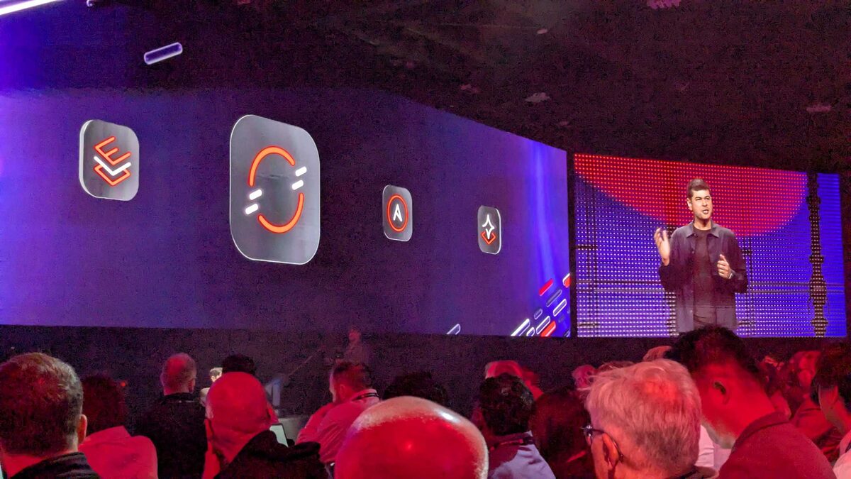 Red Hat product portfolio icons on the keynote stage — RHEL, OpenShift, Ansible, RHEL AI