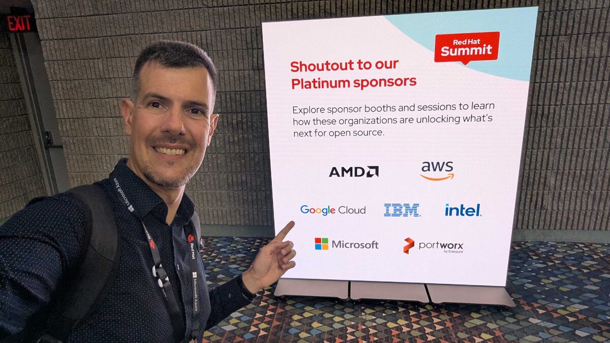 Luca Berton at Red Hat Summit 2026 with Platinum Sponsors board — AMD, AWS, Google Cloud, IBM, Intel, Microsoft, Portworx