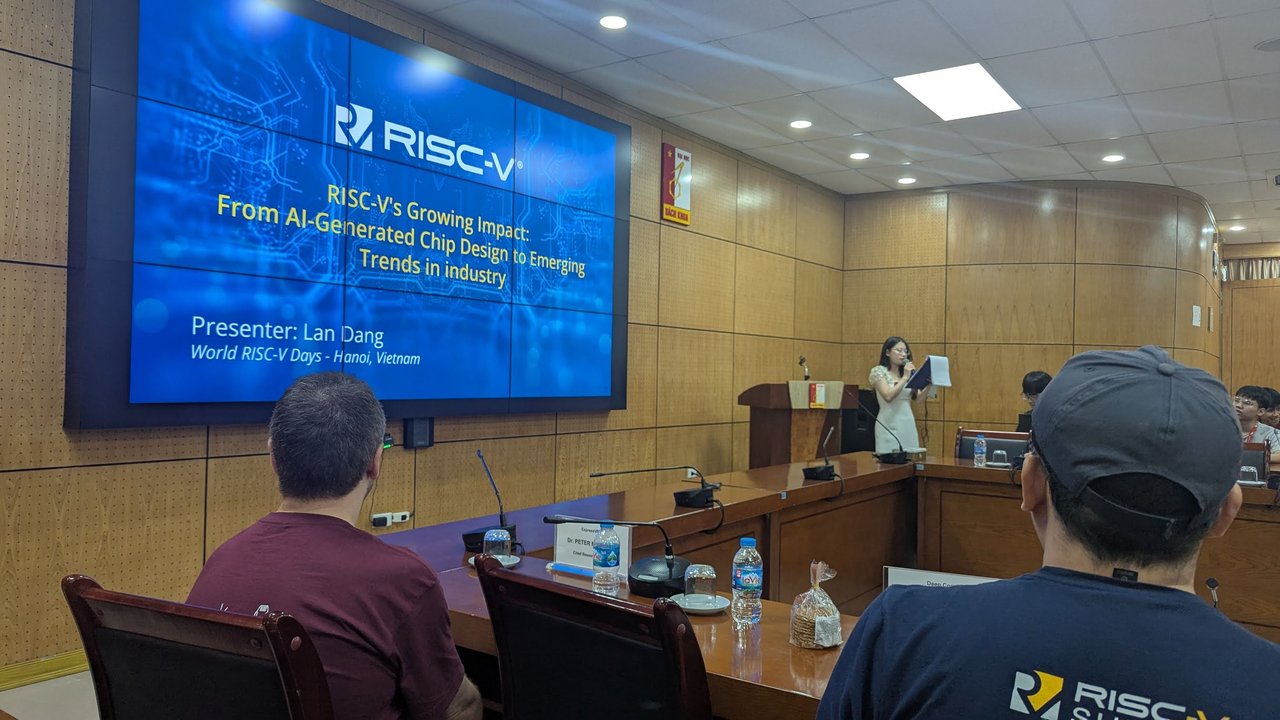 The RISC-V title slide for the talk on AI-generated chip design, with the presenter reading at the lectern