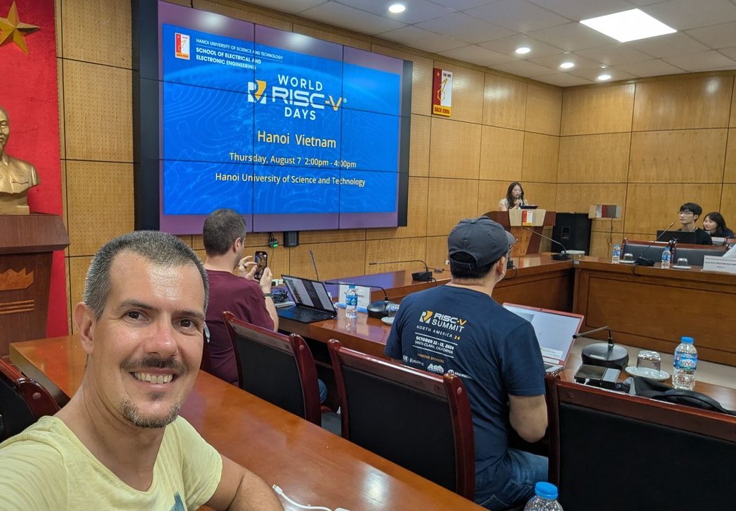Luca Berton seated in the hall at World RISC-V Days Hanoi, with the event title slide on the screen