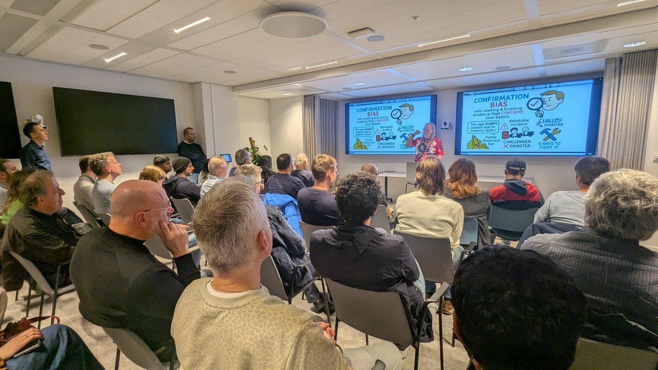 Speaker presenting the Confirmation Bias slide at the SRE NL meetup at Elastic Amsterdam, with the example This app ALWAYS crashes due to memory leaks