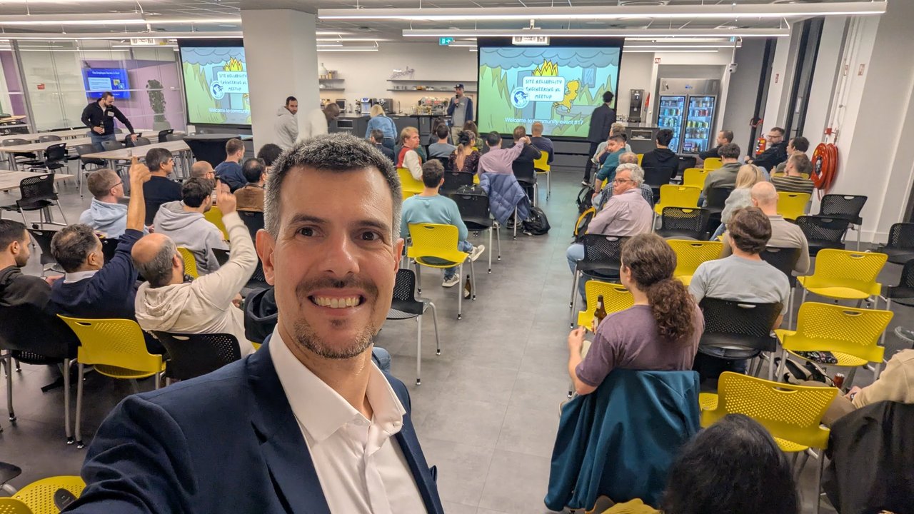 Luca Berton taking a selfie at the SRE NL meetup at the Datadog office in Amsterdam, with the audience on yellow chairs and the opening slide on two screens