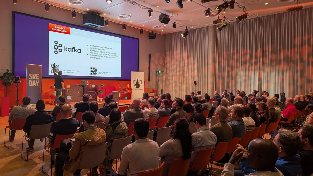 The audience at SREday watching a keynote slide titled Data is a shared asset, with the Kafka logo and three bullets about a buffer and transport layer, a persistent replayable log and a shared interface across producers and consumers