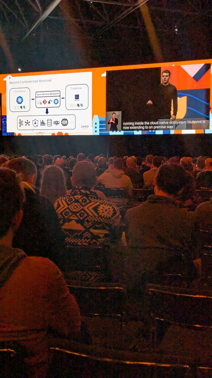 A Saxo keynote slide at KubeCon Europe 2026 titled Beyond Containerized Workload, showing a Saxo Service Blueprint box between Cloud Native and Traditional workloads, with an arrow down to a row of platform services