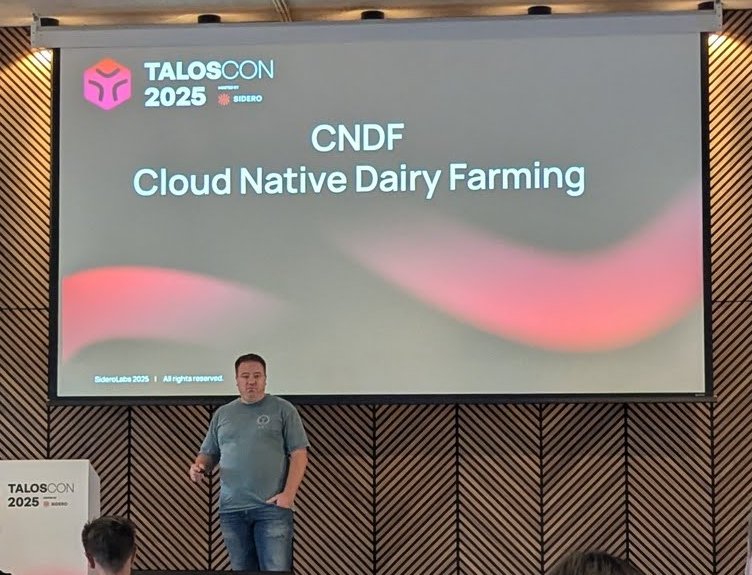 Cloud Native Dairy Farming title slide at TalosCon 2025 with the speaker on stage