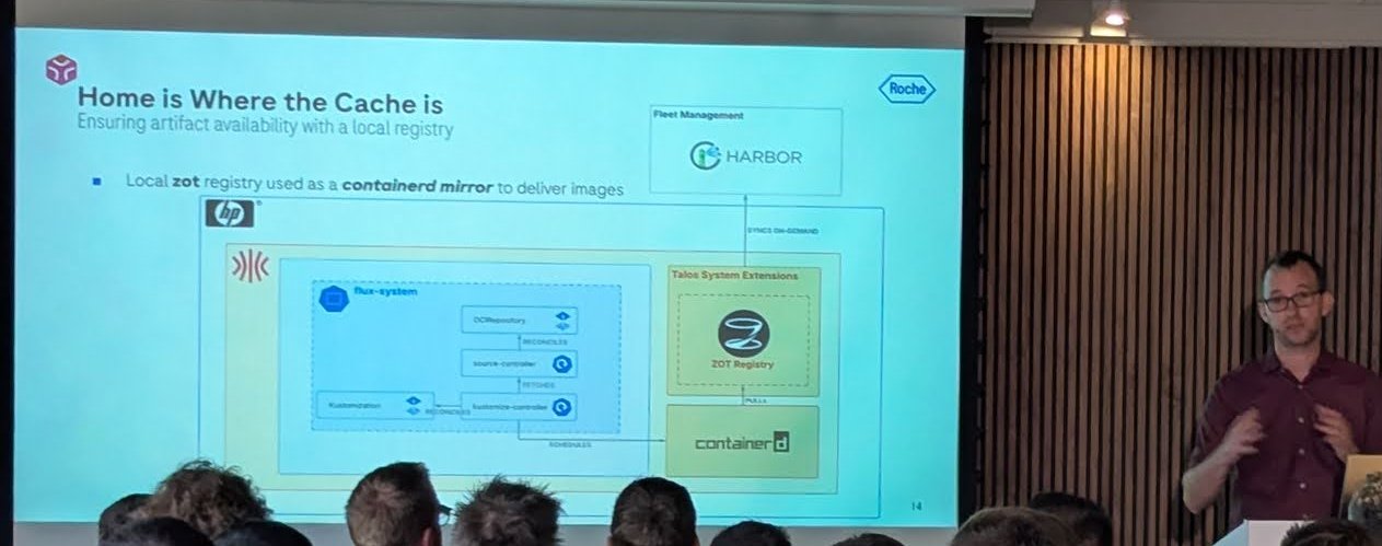 Roche slide Home is Where the Cache is, showing a local zot registry running as a Talos system extension and acting as a containerd mirror, with Flux controllers and a central Harbor registry