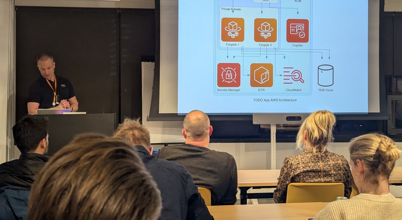 The AWS speaker at the lectern next to a TODO App AWS Architecture diagram: Fargate 1 and Fargate 2 in private subnets, Cognito, Secrets Manager, ECR, CloudWatch and TiDB Cloud