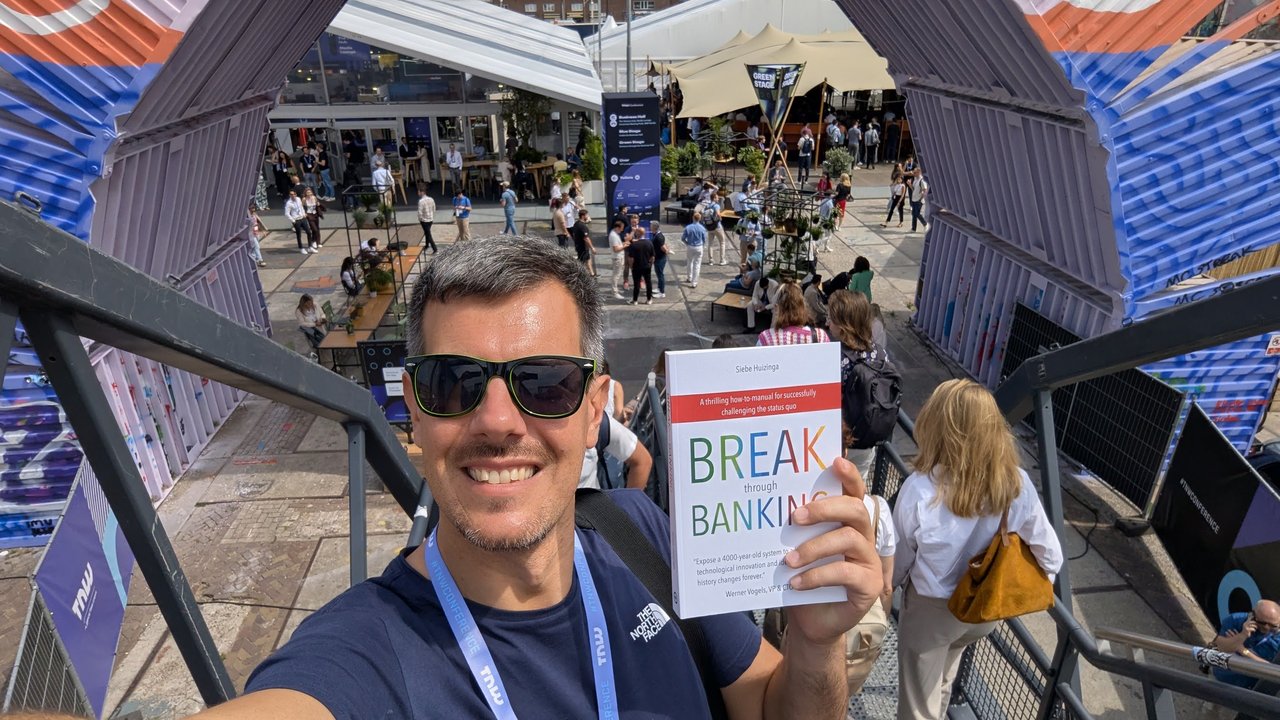 Luca Berton holding the book Break Through Banking on a metal staircase above the TNW Conference courtyard