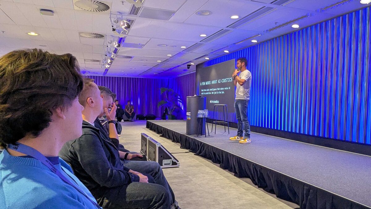 ai-coustics presentation — "Real-time audio intelligence that makes voice AI work in production. Not just in the lab." — speaker on stage with engaged audience