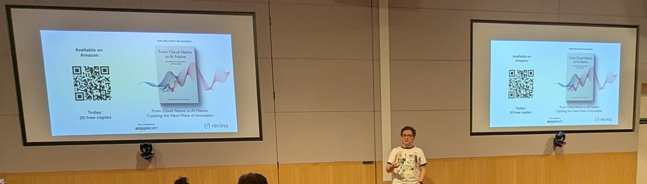 Pini Reznik on stage between two screens showing the slide Available now on Amazon, From Cloud Native to AI Native: Catching the Next Wave of Innovation, Today: 20 free copies