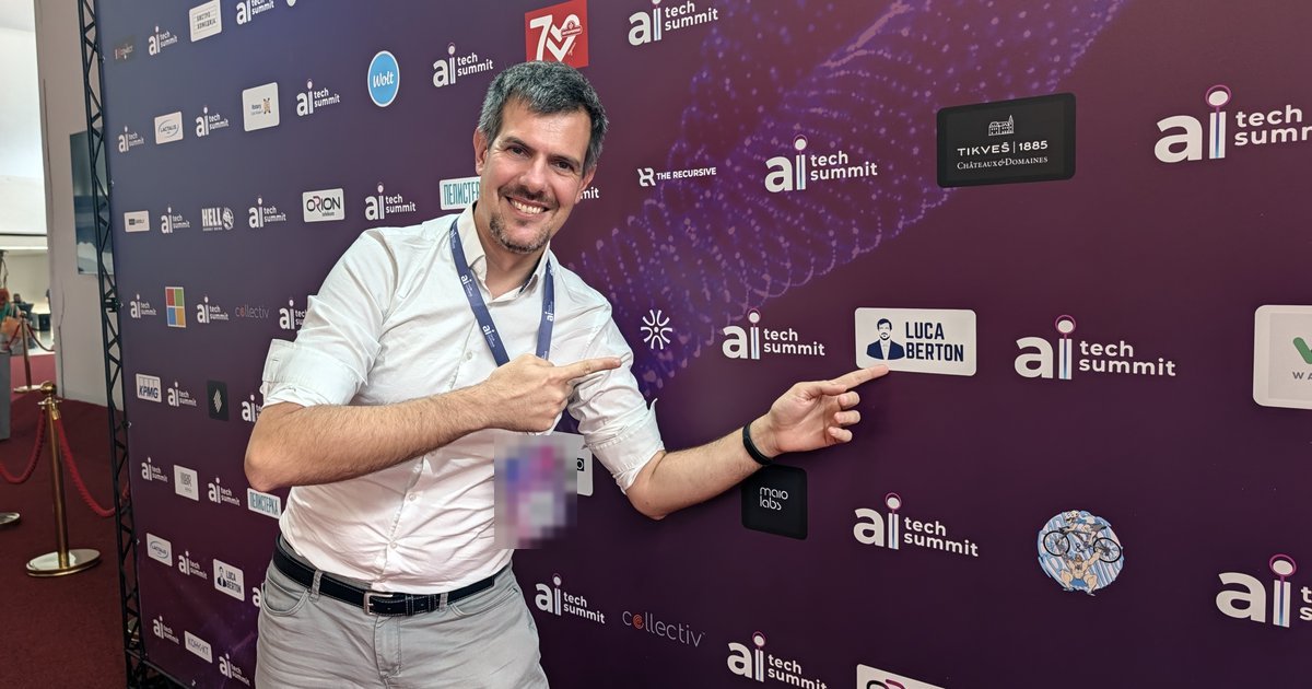 Luca Berton pointing at his LUCA BERTON speaker card on the AI Tech Summit sponsor wall in Skopje