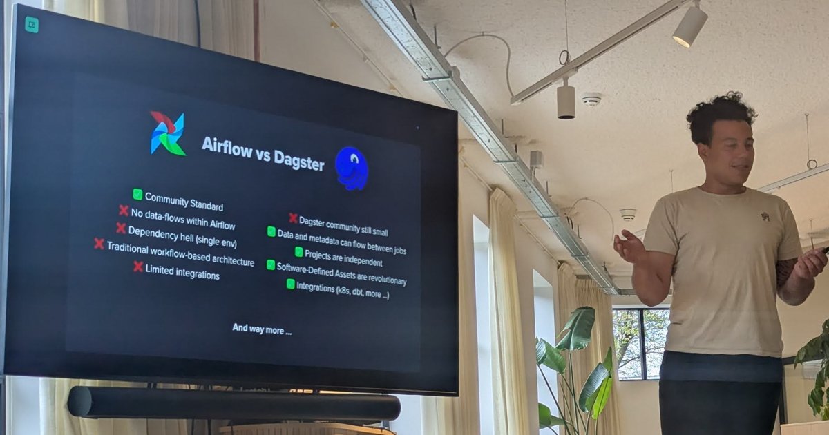 A speaker presenting an Airflow vs Dagster comparison slide on a screen at an Amsterdam.dev meetup