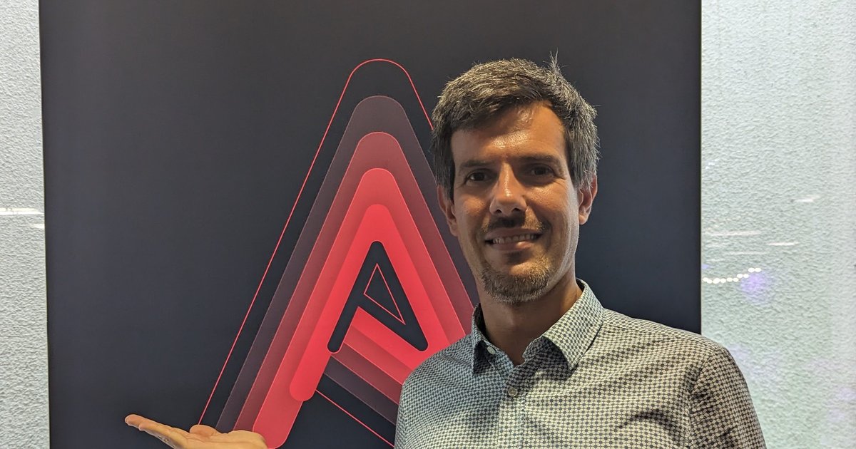 Luca Berton presenting the large red Ansible A logo on a dark wall at Ansible Automates London 2023