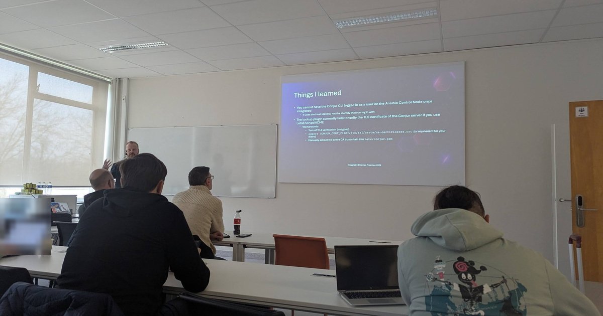 James Freeman presenting a Things I learned slide about Ansible and CyberArk Conjur in a classroom at CfgMgmtCamp 2025 in Ghent