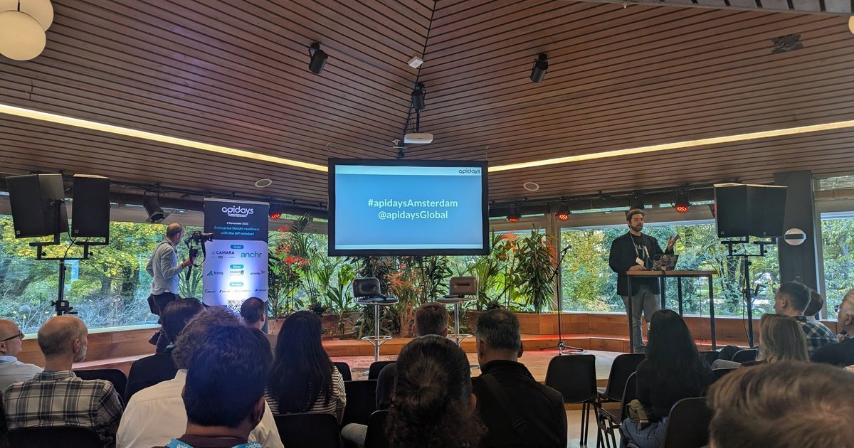 The Apidays Amsterdam 2025 main room at Tolhuistuin with a speaker at the lectern and the hashtag slide on the screen