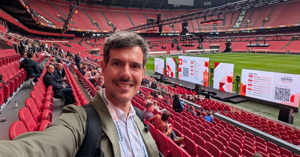 Luca Berton taking a selfie in the stands of the Johan Cruijff ArenA, with the Databricks stage and agenda screens on the pitch