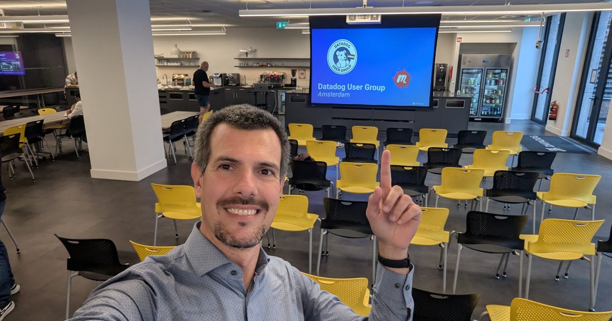Luca Berton at the Datadog office in Amsterdam, in front of the Datadog User Group Amsterdam opening slide and rows of yellow chairs