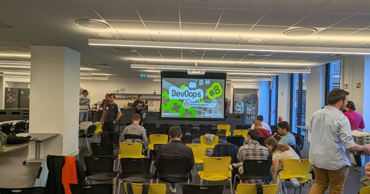 Attendees mingling before the talks at DevOops #8 with Amsterdam.dev at the Datadog office in Amsterdam, with the DevOops #8 slide on the screen
