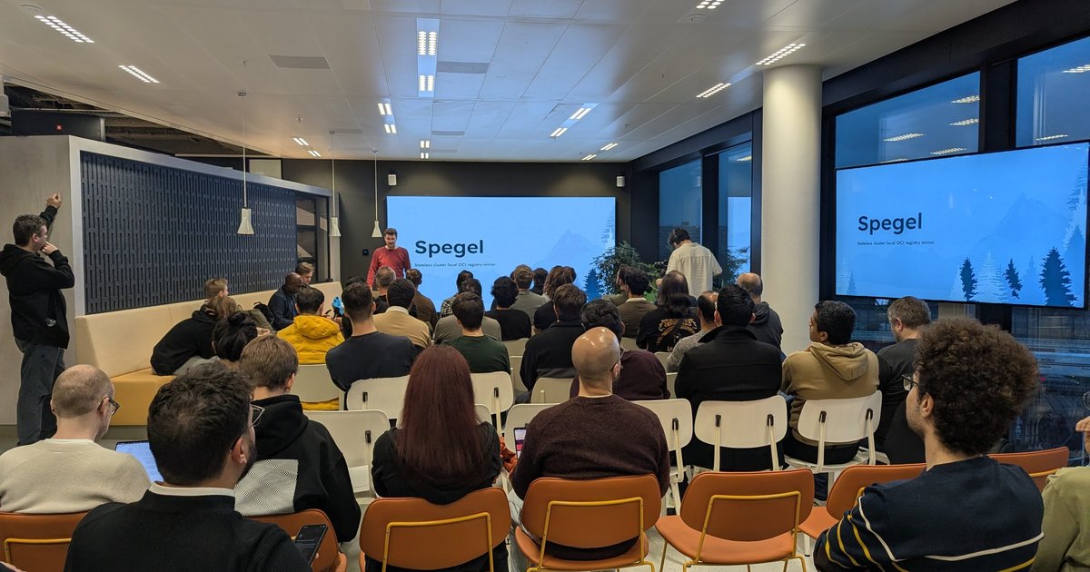 Audience at the Dutch Cloud Native & AI Community Group meetup facing two screens showing the Spegel title slide