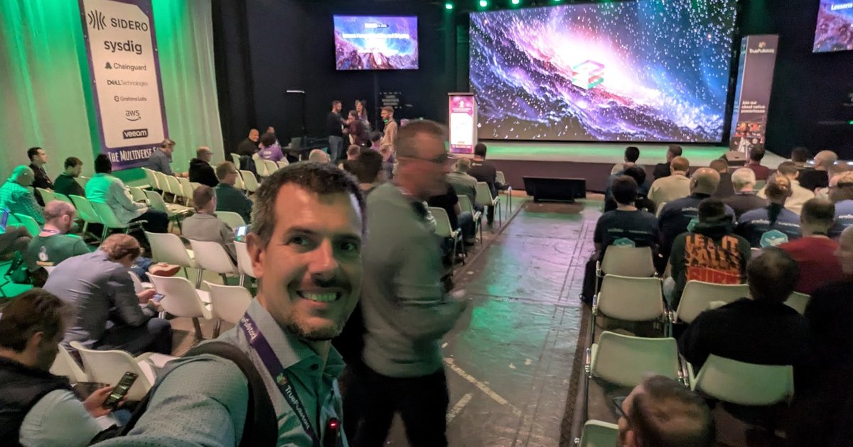 Luca Berton in the main hall of EDGECASE 2025 in Amersfoort, with a sponsor banner and a large LED wall showing a galaxy behind him