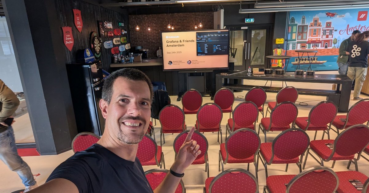 Luca Berton pointing at the Grafana & Friends Amsterdam, Sep 24th 2025 title slide in a room of red chairs