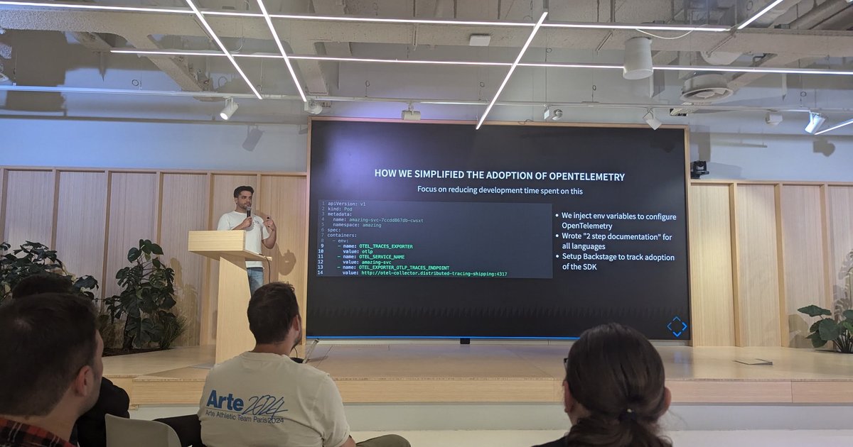 A speaker on stage next to a slide titled How we simplified the adoption of OpenTelemetry