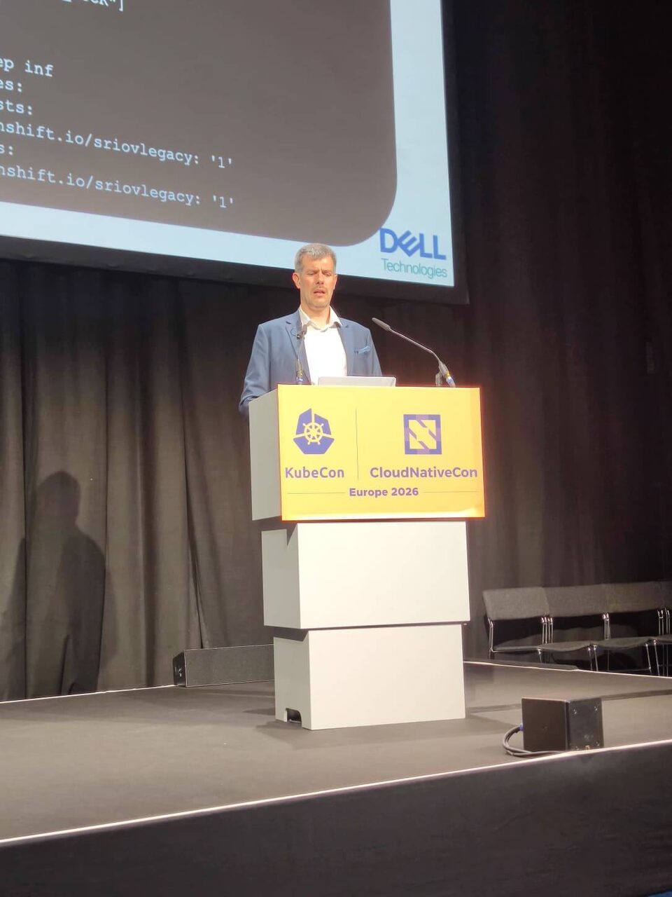 Luca Berton at the podium showing SR-IOV legacy configuration code on screen