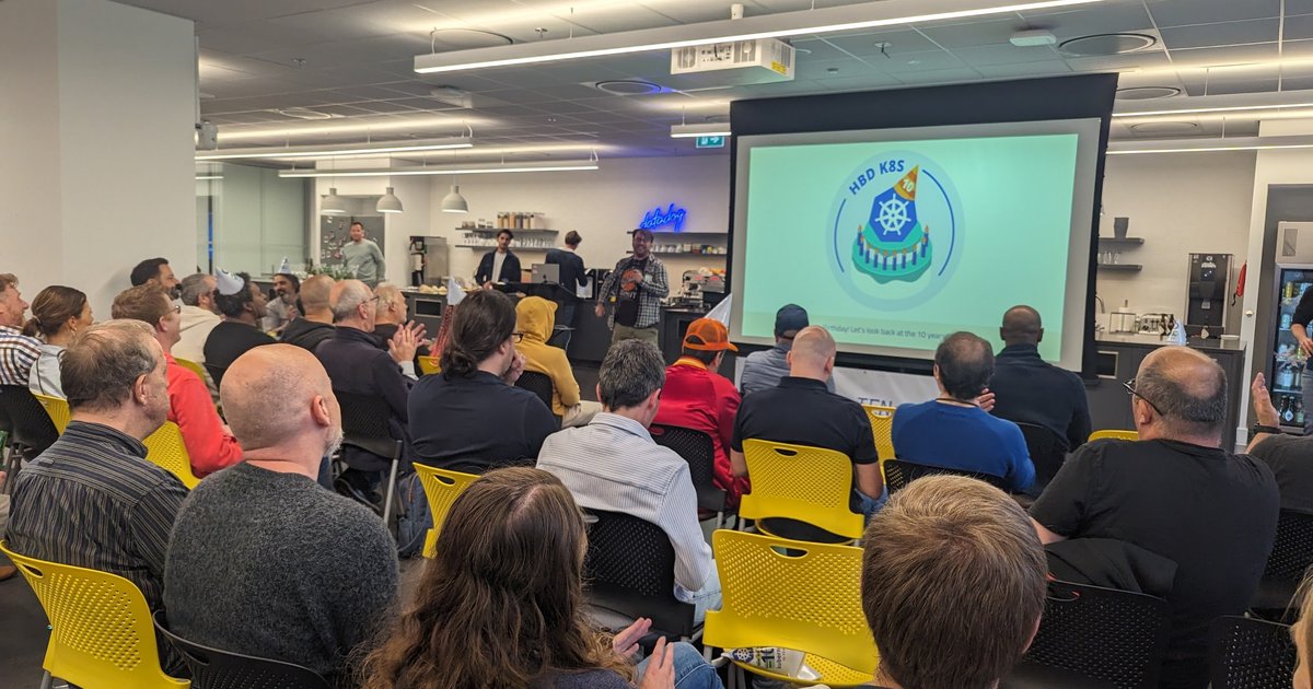 A Happy Birthday Kubernetes slide with a party-hat logo on screen in a meetup room at Datadog in Amsterdam