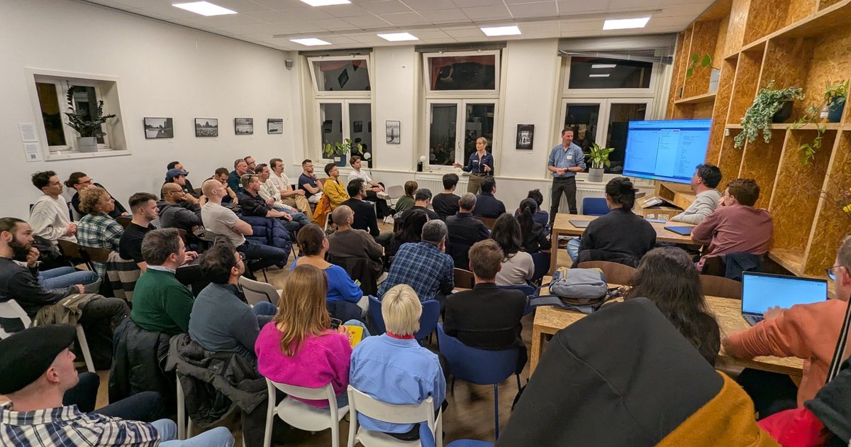 A full room at the n8n meetup in Amsterdam, with two presenters at the front next to a screen showing a workflow