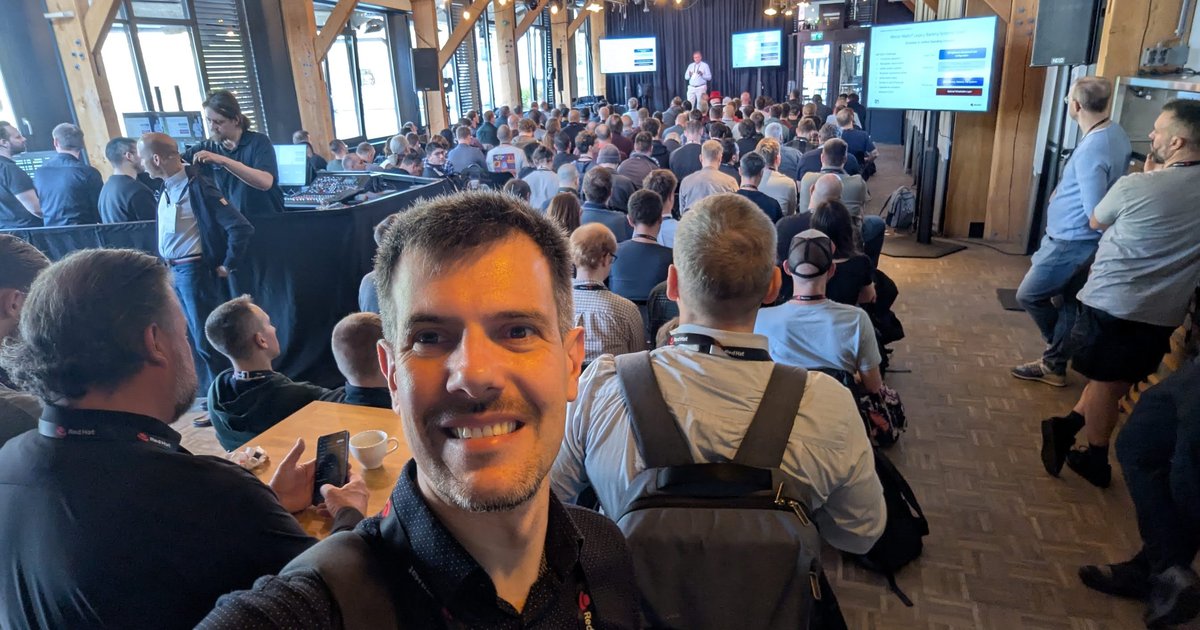 Luca Berton in the packed main room at OpenShift Commons Gathering Amsterdam 2026, with a speaker on stage and slides on the screens