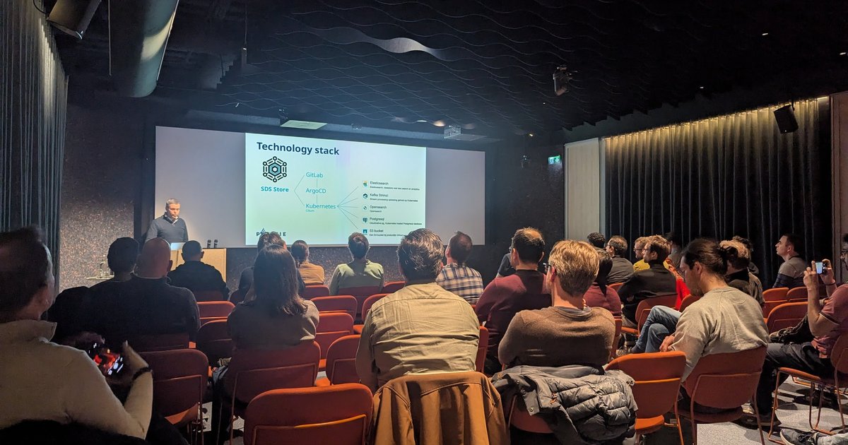Audience at a PostgreSQL user meetup in Amsterdam watching a Technology stack slide for the Politie SDS Store platform