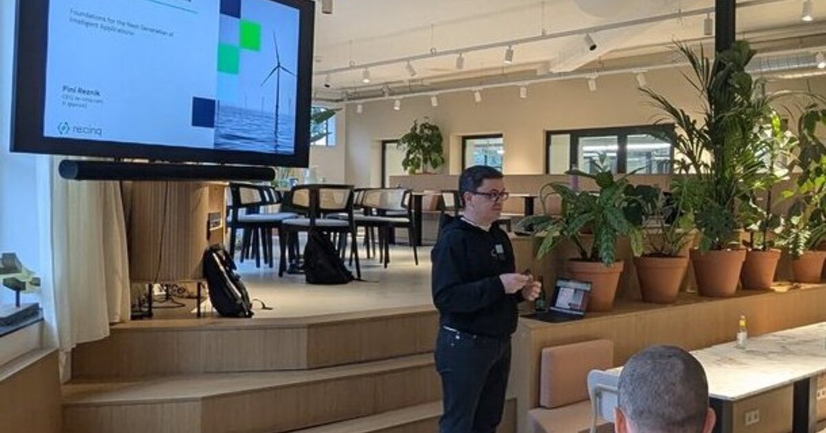 A speaker presenting the Building AI-Native Platforms title slide to an audience seated around tables in an Amsterdam meetup room